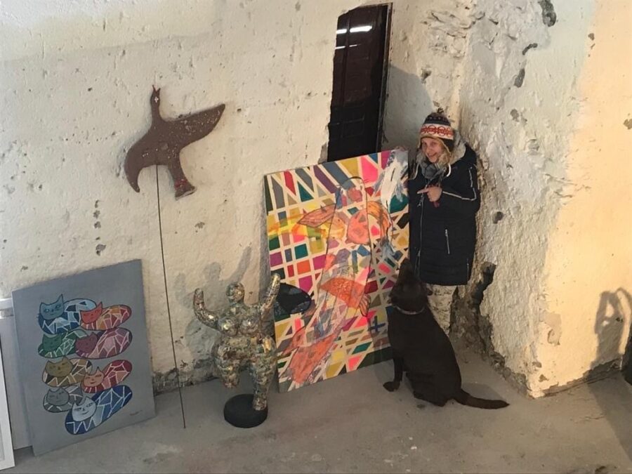 Priska Schwab è in piedi davanti a una delle sue foto con il suo Labrador marrone e la indica.