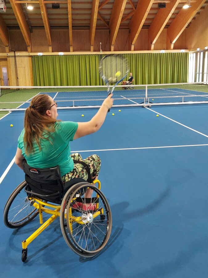Donna che gioca a tennis su una sedia a rotelle speciale.